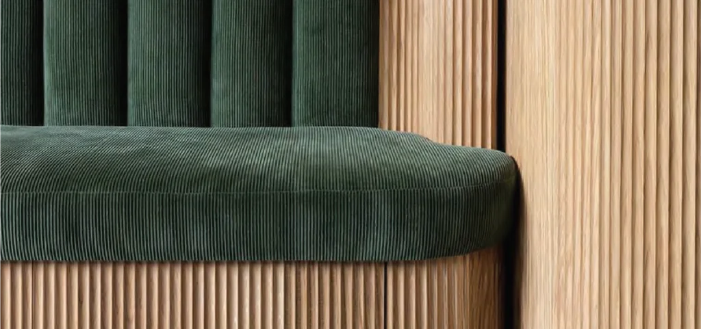Close-up view of a seating area with green ribbed fabric upholstery and a light wood base featuring vertical slatted louver details.