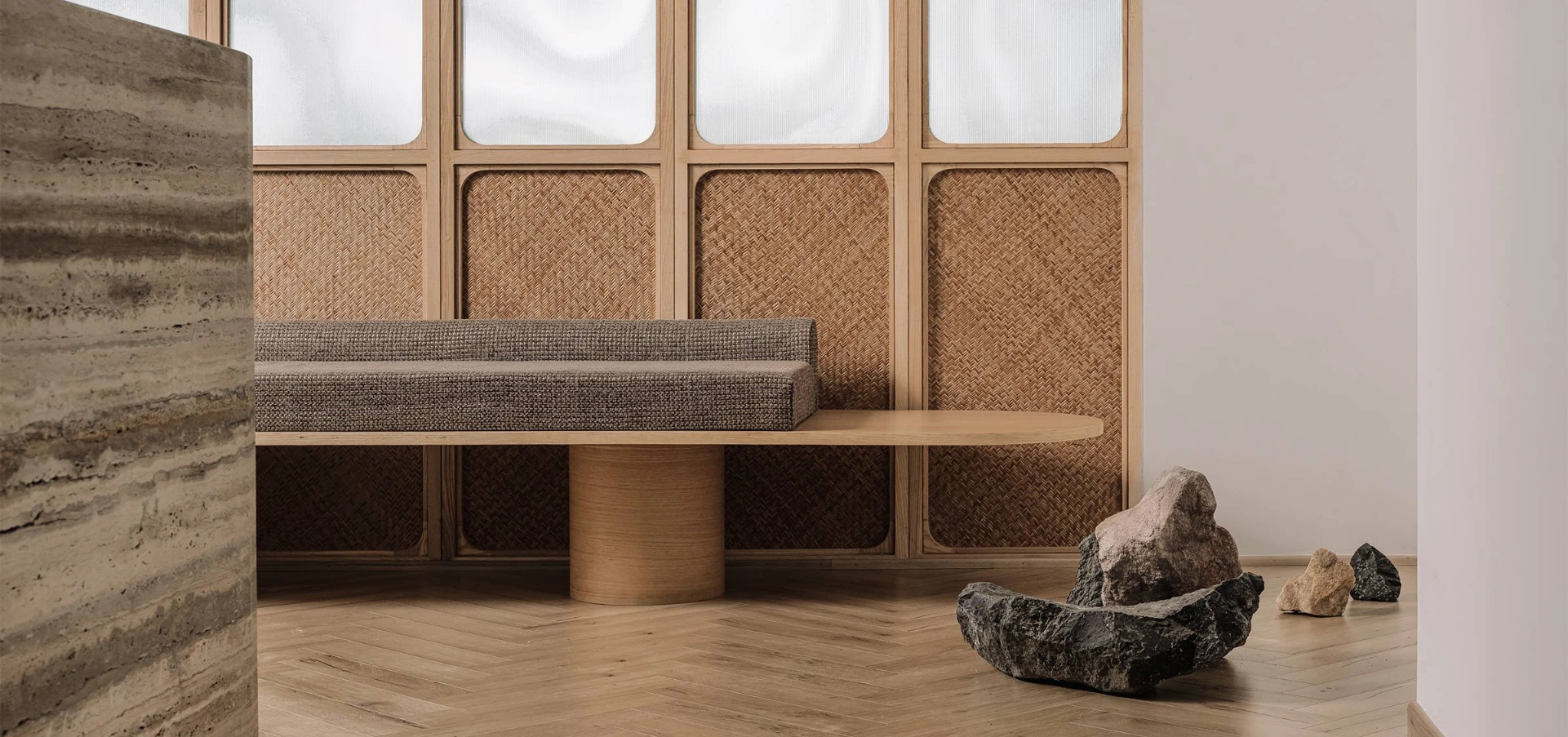 Interior seating area with rattan cane wall panels and minimalistic decor featuring natural rocks and wooden accents.