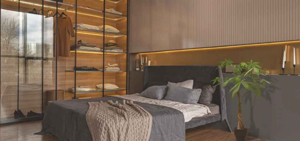 Modern bedroom with Flava Acrylic wardrobe showcasing wooden shelves and glass sliding doors, a dark upholstered bed, and warm lighting accents.