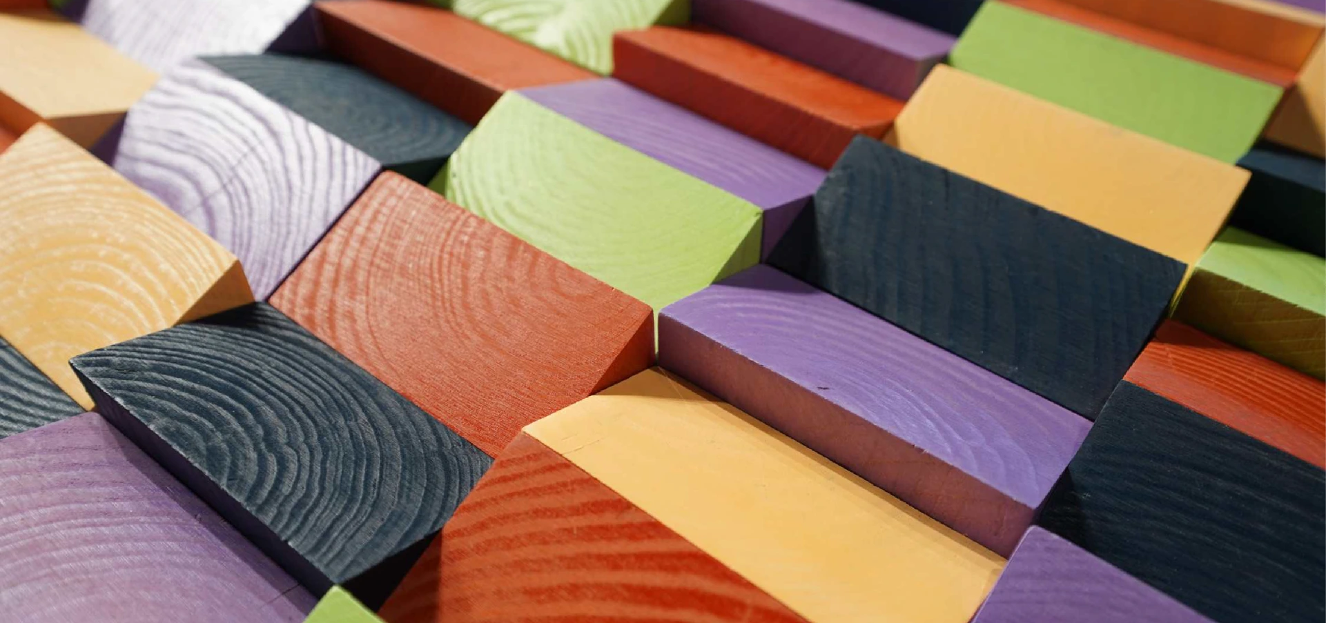 Close-up of a vibrant multicolored wooden mosaic featuring angled, textured wood pieces in shades of red, green, orange, and purple.